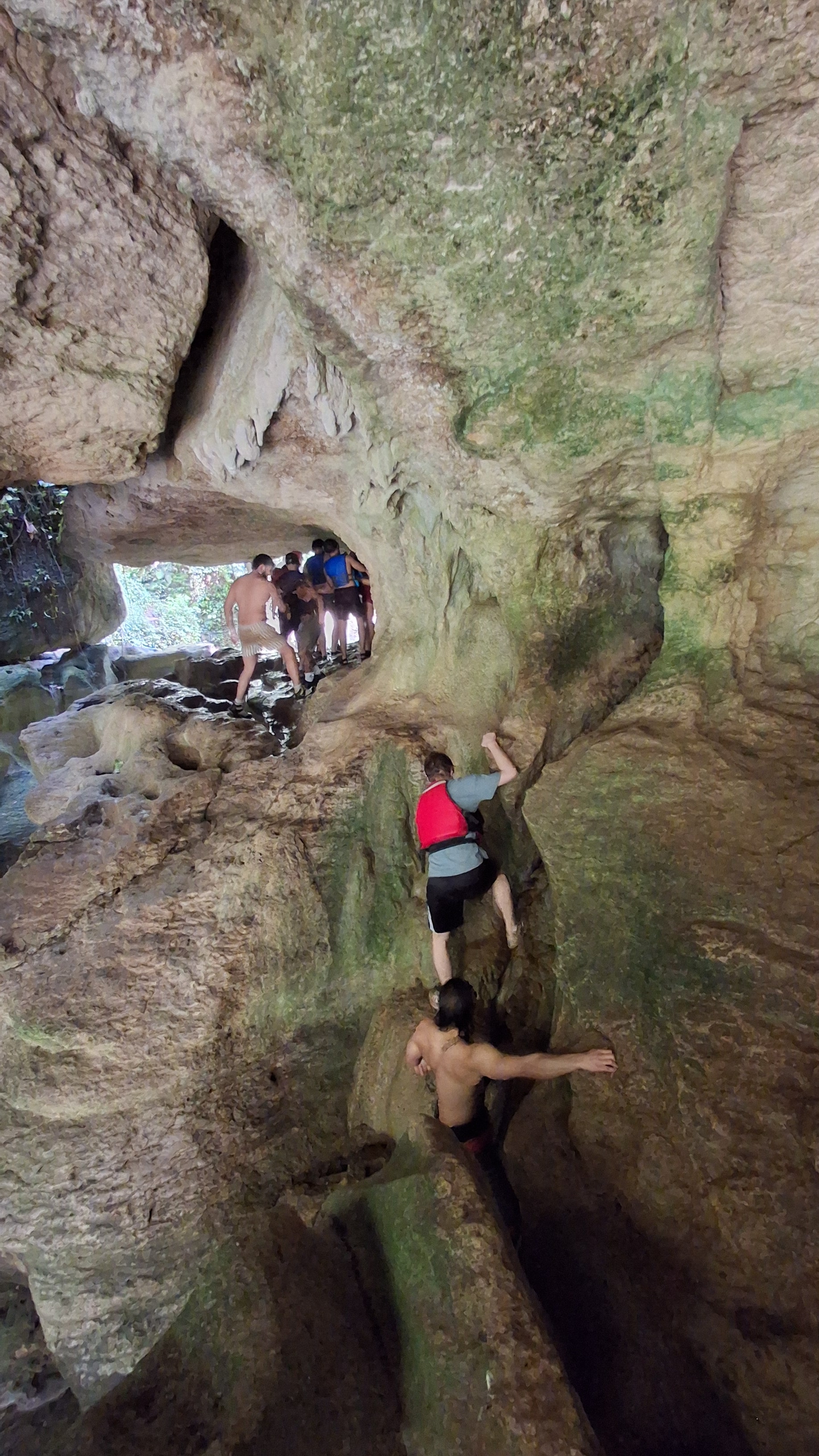 Guests climbing through a mossy rock passage inside the karst cave